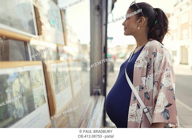 Pregnant woman browsing real estate listings at urban storefront