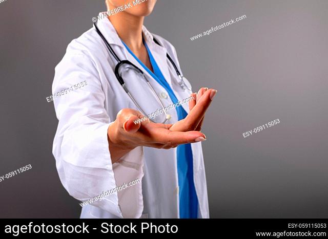 Mid section of female doctor with cupped hand against grey background