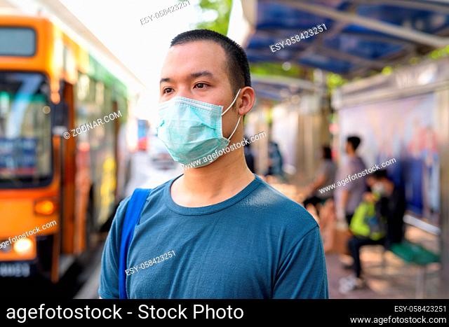 Portrait of young Asian man with mask for protection from corona virus outbreak at the bus stop in the city outdoors