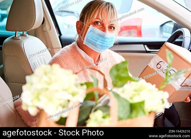 Frau mit Mundschutz in Auto Innenraum hält Paket eines Lieferservice in den Händen