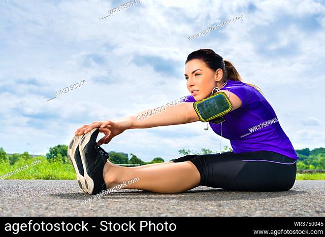 Urban sports - young woman is doing warming up before running in the greenfield on a summer day