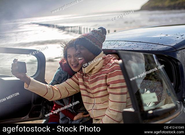 Happy playful couple taking selfie at car on winter beach