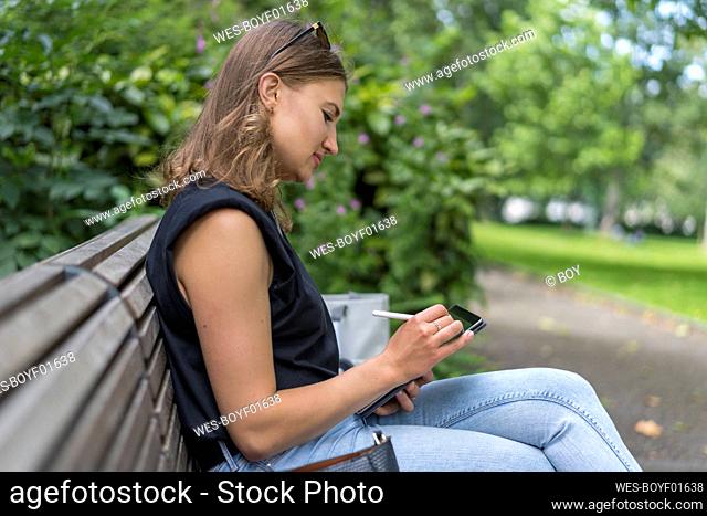 Young woman drawing on graphic tablet while sitting in public park