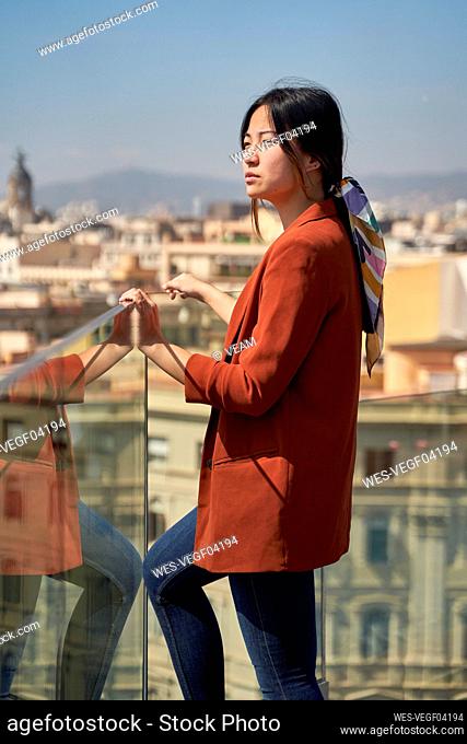 Young woman looking at view while standing by glass railing on roof terrace