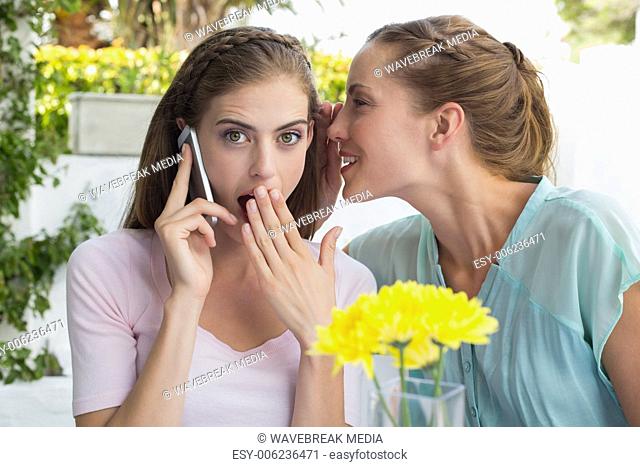 Woman whispering secret into friends ear while shes on call