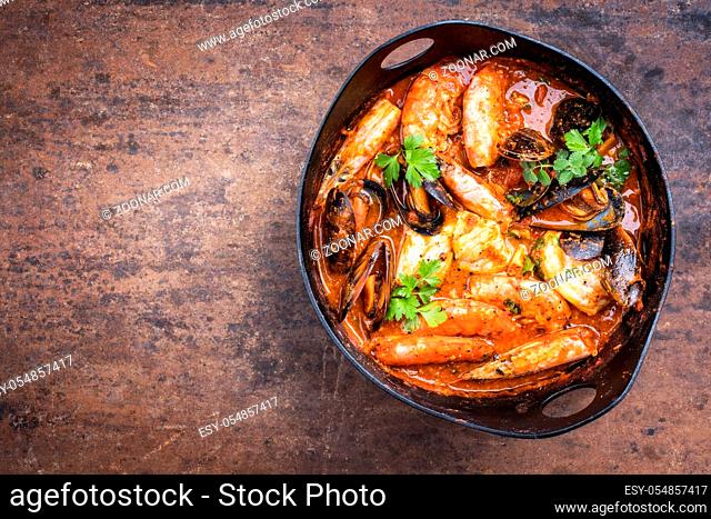 Traditional Catalan fish stew romesco de peix with prawns, mussels and fish as top view in a modern design cast-iron roasting dish with copy space left