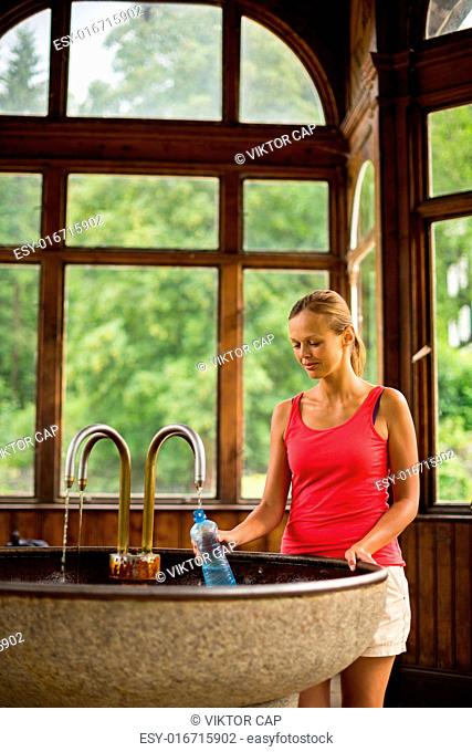 Young woman fillig a plastic bottle with healthy mineral water from a wellspring in a spa (shallow DOF)