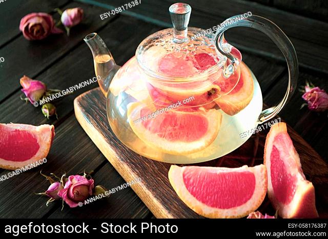 Pink grapefruit herbal tea with ginger and honey in a glass teapot on dark background