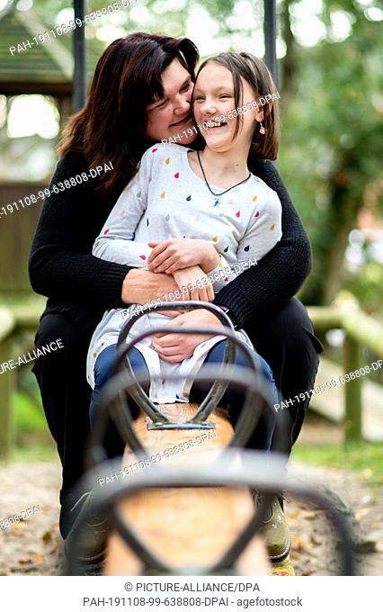 14 October 2019, Lower Saxony, Löningen: Kathrin Schenk and her daughter Tabea are sitting on a seesaw on a playground. When her daughter Tabea starts blinking...