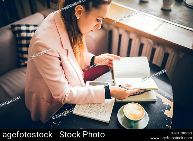 Working comfortably at a cafe. Woman freelancer leafing through pages of a diary in a coffee shop. Attractive woman drinking coffee on restaurant terrace with...