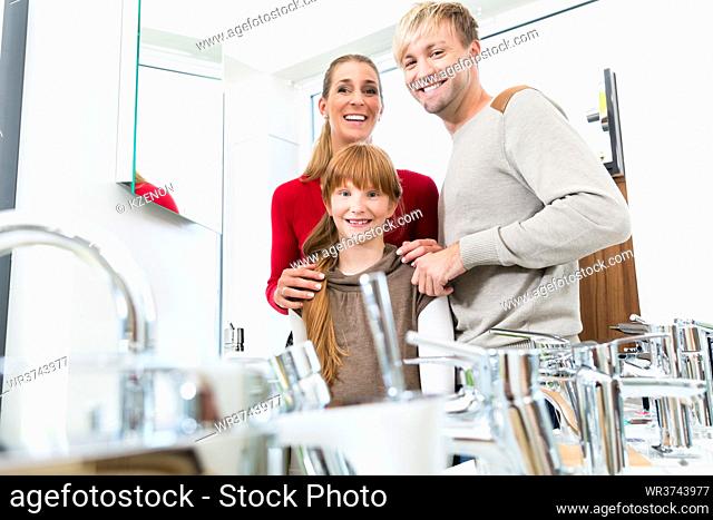 Portrait of a happy family with one child looking at camera, while posing together in the interior of a modern sanitary ware shop with various bathroom faucets...