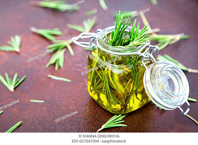 Rosemary oil. Rosemary essential oil jar glass bottle and branches of plant rosemary with flowers on rustic background