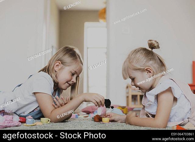 Close-up of female children playing with colorful toy play tea set. Kids lying at home bedroom or kindergarten, nursery. Educational eco-friendly game for child