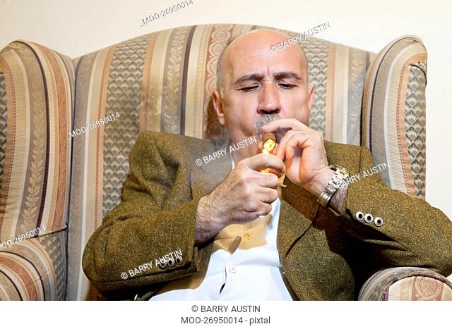 Mature man igniting cigar while sitting on armchair
