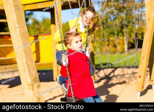 Family with Mother and daughter swinging and playing on play area or court
