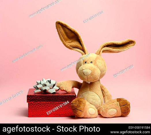 cute plush rabbit holding a red gift box, pink background