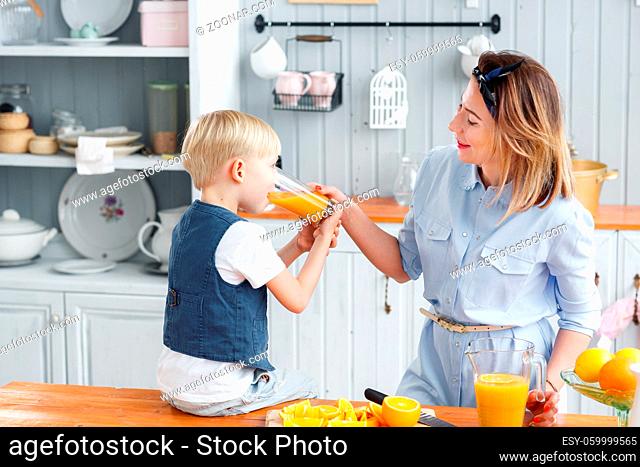 son and young mother in the kitchen eating Breakfast. Boy drinking orange juice. Healthy food concept