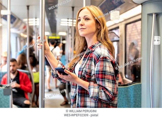 Smiling woman with smartphone on the subway, Berlin, Germany