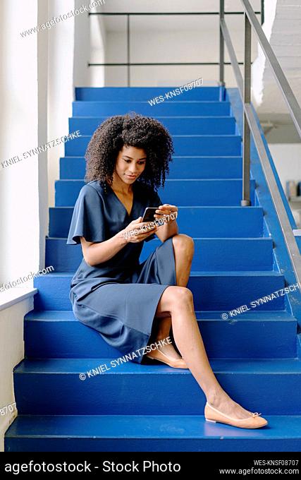 Businesswoman using smart phone while sitting on steps at office