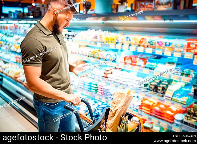 Man choosing dairy products in grocery store. Male person with cart buying beverages and products in market, customer shopping food and drinks in supermarket