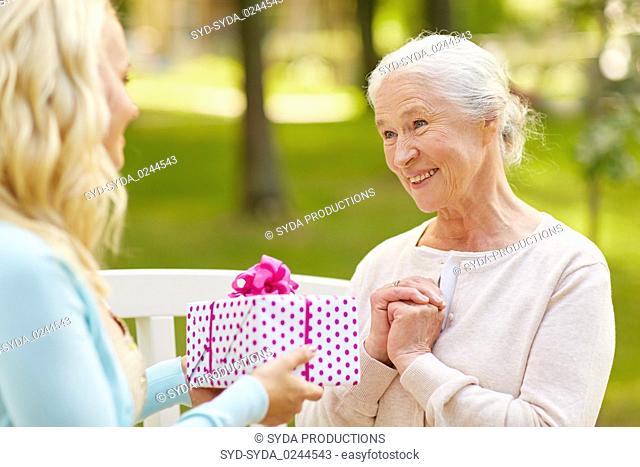 daughter giving present to senior mother at park