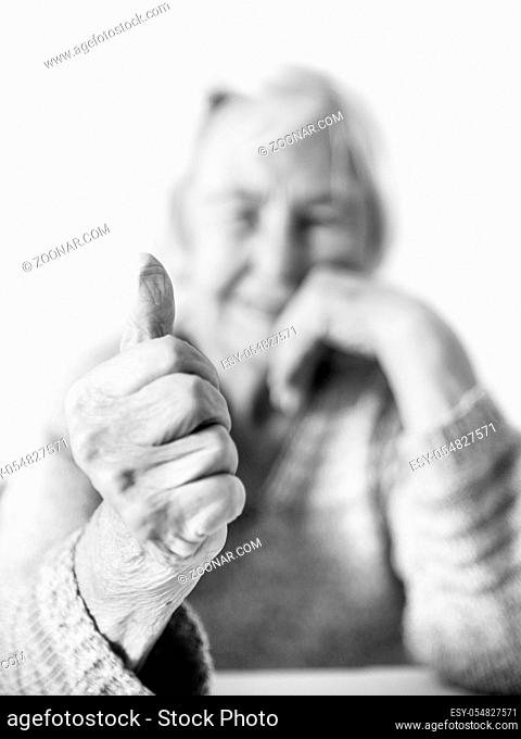 Content 96 years old elderly woman giving a thumb up and looking at camera. Focus on the thumb up, face out of focus. Old age and the quality of life concept