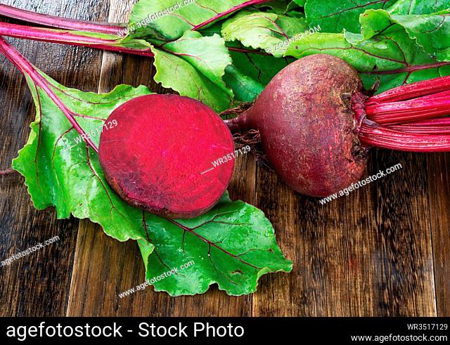 Fresh beetroots with leaves on wet wooden rustic table.Whole and cut beetroots