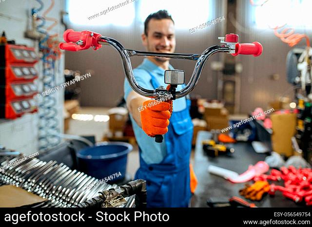 Bicycle factory, worker shows girl's bike handlebar. Male mechanic in uniform installs cycle parts, assembly line in workshop, industrial manufacturing