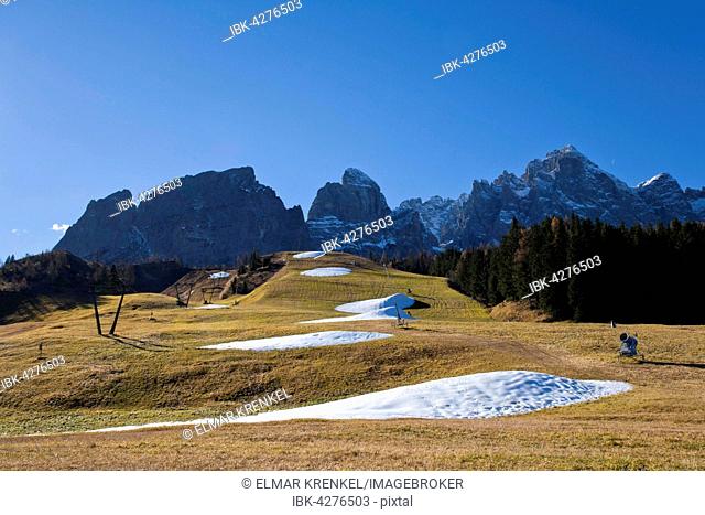 Snowmaking system in the fall, brown meadow with piles of snow, behind mountains with snow, Passo Monte Croce, Sexten Dolomites, Province of South Tyrol, Italy