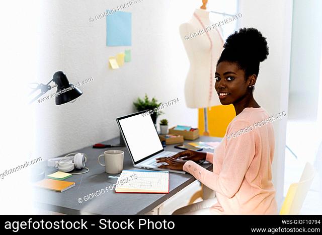 Smiling fashion designer using laptop while sitting at home office