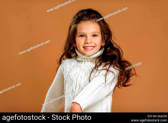 happy smiling little child girl in white sweater looking to camera on beige background. Human emotions and facial expression
