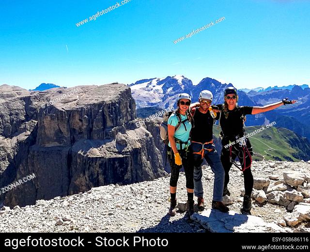 A mountain guide and two female climbers celebrate standing on the summit after a climb