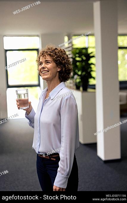 Happy businesswoman standing with glass of water in office