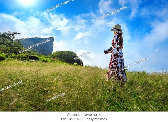 Woman standing on meadow and holding camera at Phu Chi Fa mountains in Chiangrai, Thailand. Travel concept