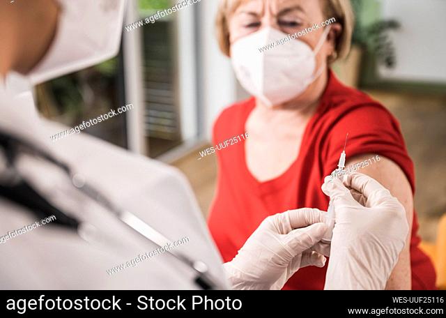 Doctor holding vaccine injection with woman in background at home