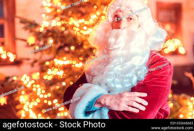 Santa Claus posing in front of a Christmas tree outdoors