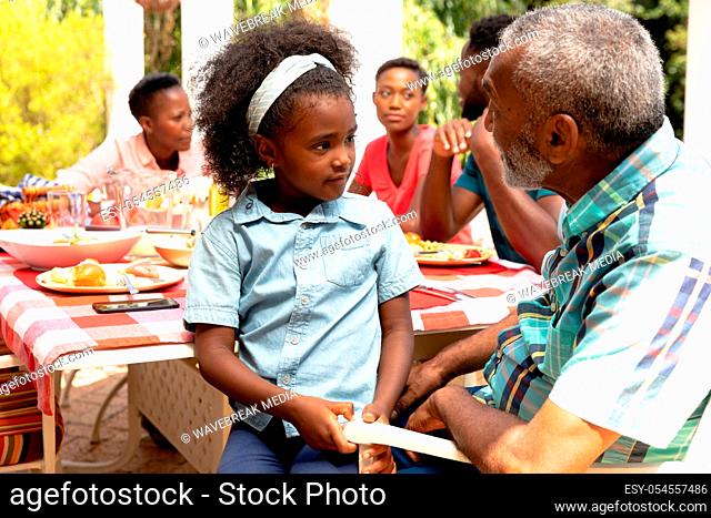 African American girl sitting on her grandfather knees during a family lunch in the garden