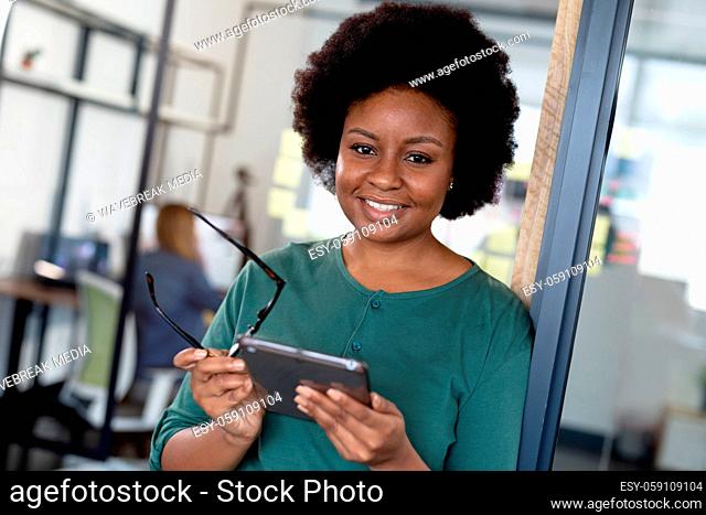 Portrait of happy african american businesswoman holding glasses and digital tablet
