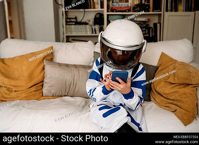 Girl wearing space costume using smart phone on sofa in living room