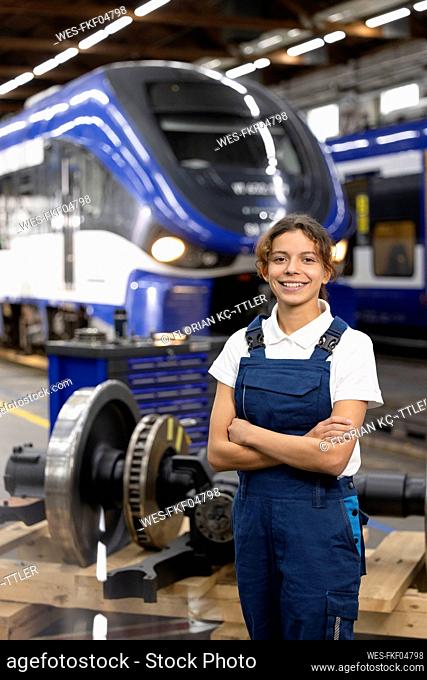 Smiling young trainee standing with arms crossed in warehouse at industry
