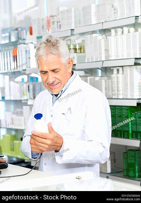 Smiling male pharmacist scanning barcode of shampoo bottle at counter in pharmacy