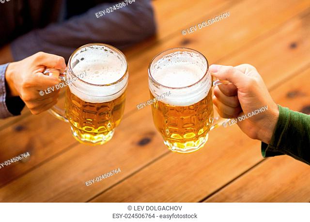 people, leisure and drinks concept - close up of male hands clinking beer mugs at bar or pub