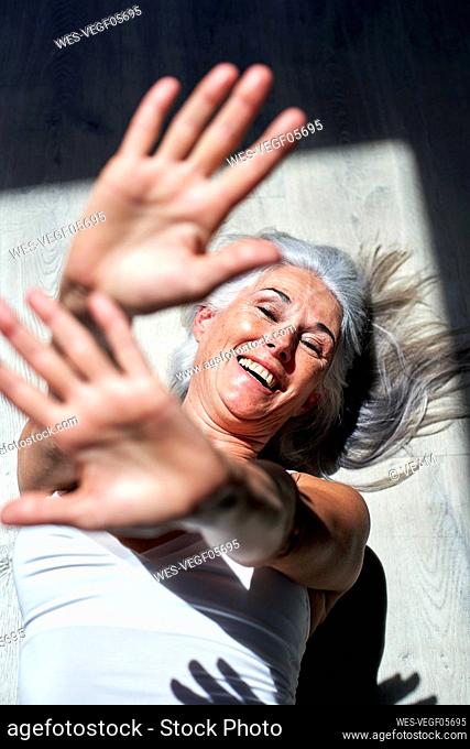 Happy mature woman with hands raised lying on floor