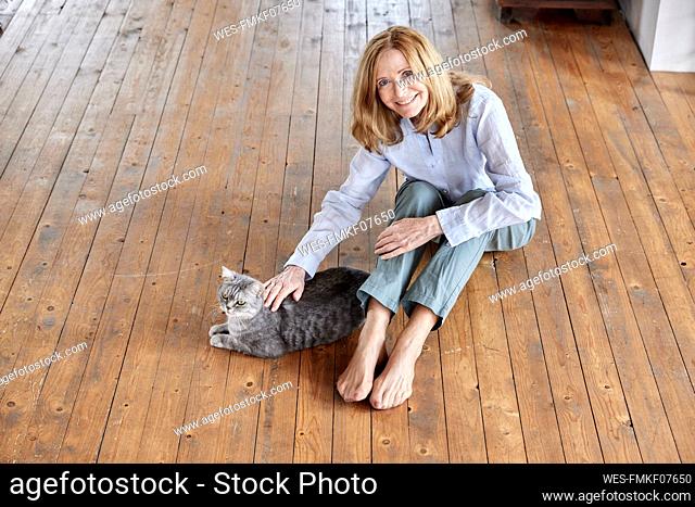 Smiling woman with cat sitting on floor at home