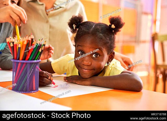 Afrikanisches Mädchen malt mit Buntstiften auf Papier ein Bild im internationalen Kindergarten