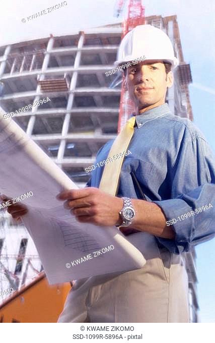 Portrait of an engineer standing at a construction site holding blueprints