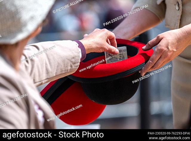 20 May 2023, Saxony, Chemnitz: A visitor throws money into a hat at the Hat Festival in downtown Chemnitz. The event, now in its sixth edition