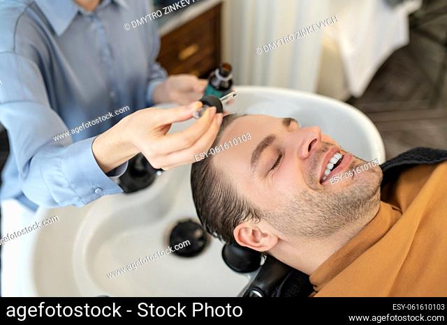 Hair revitalization. Beautician applying hair serum on mans head