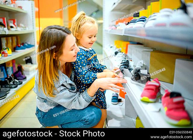 Mother and little baby looking on shoes in kid's store. Mom and adorable girl near the showcase in children's shop, happy childhood
