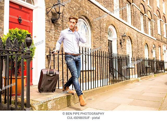 Businessman leaving house with wheeled suitcase, London, UK